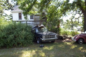 old house and truck surrounded by overgrown bushes