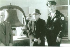 black and white photo of men standing in front of a bell