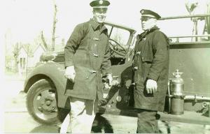black and white photo of two firefighters standing in front of a truck